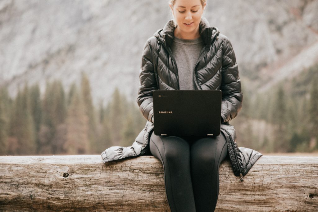 Žena sedí v přírodě s laptopem na klíně.
