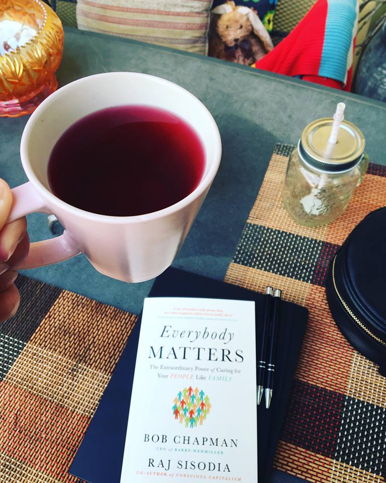 Hrnek s čajem na stole s knihou Everybody matters.